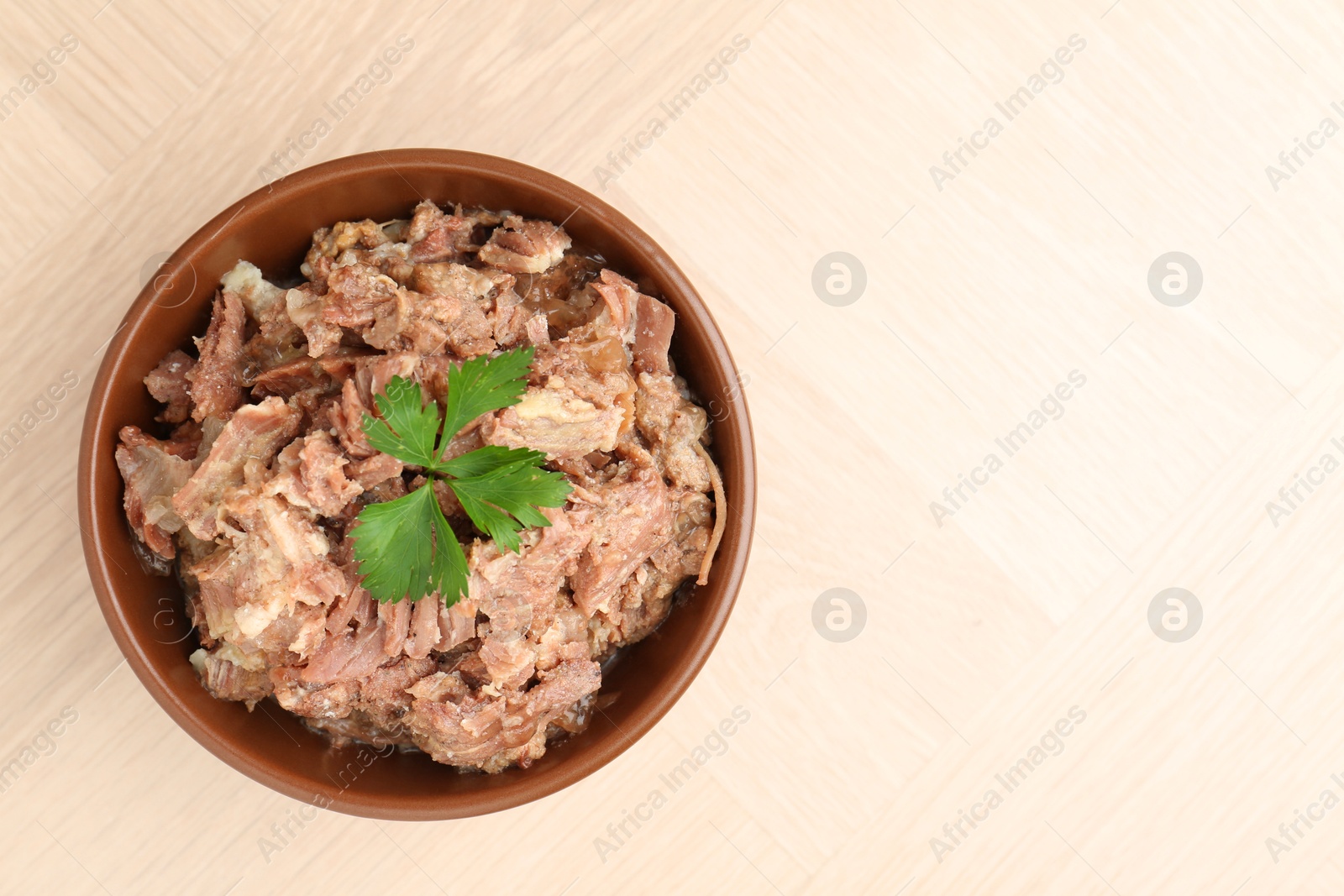 Photo of Canned meat with parsley in bowl on wooden table, top view. Space for text