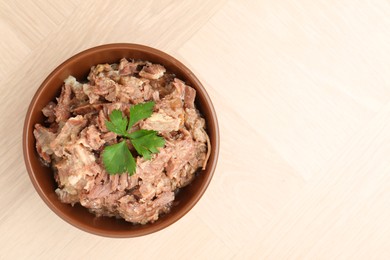 Photo of Canned meat with parsley in bowl on wooden table, top view. Space for text