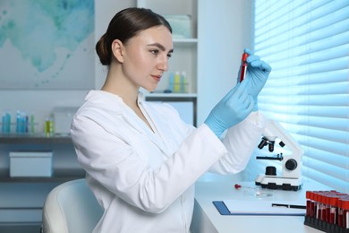 Laboratory testing. Doctor holding test tube with blood sample at table indoors