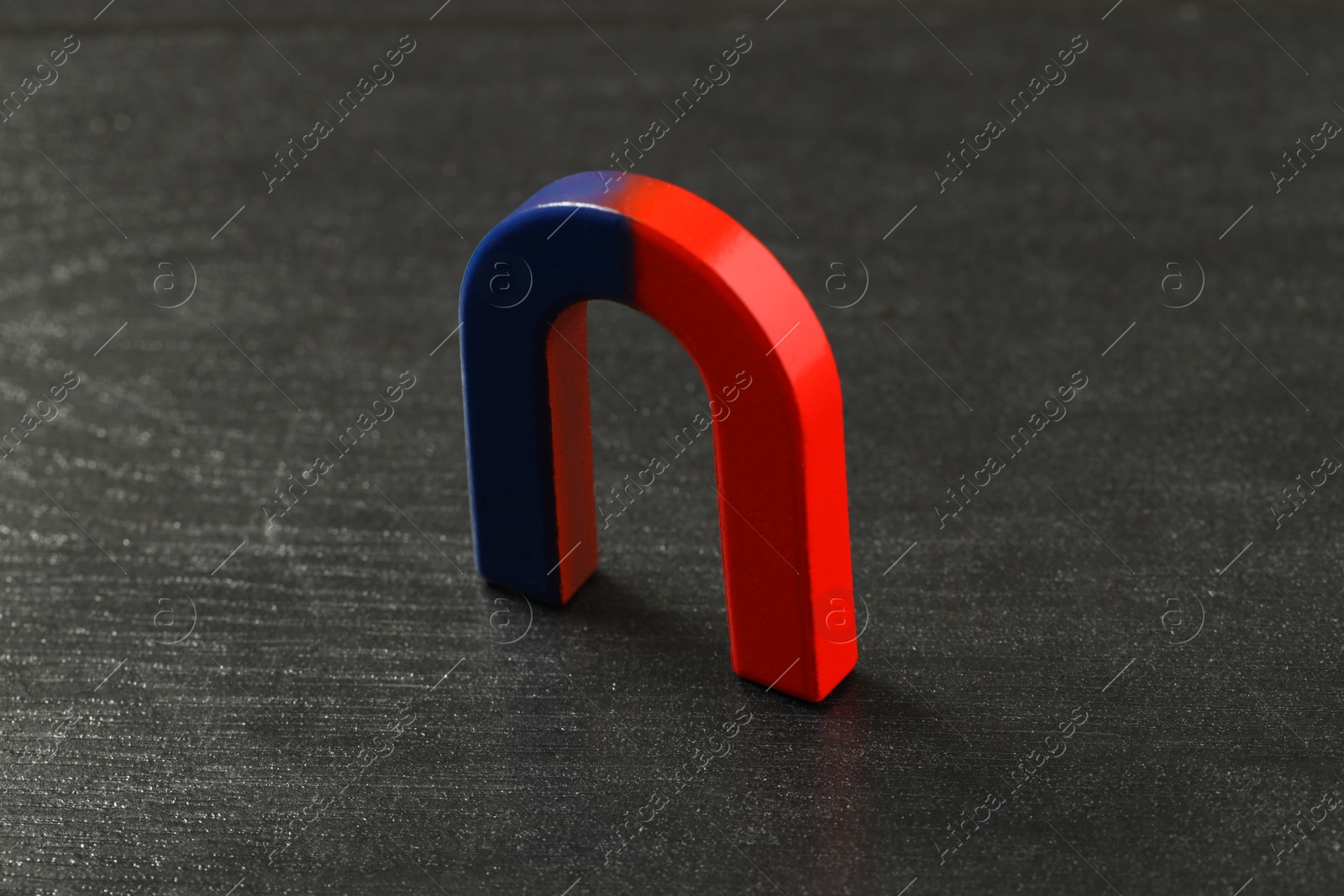 Photo of One horseshoe magnet on black wooden table, closeup