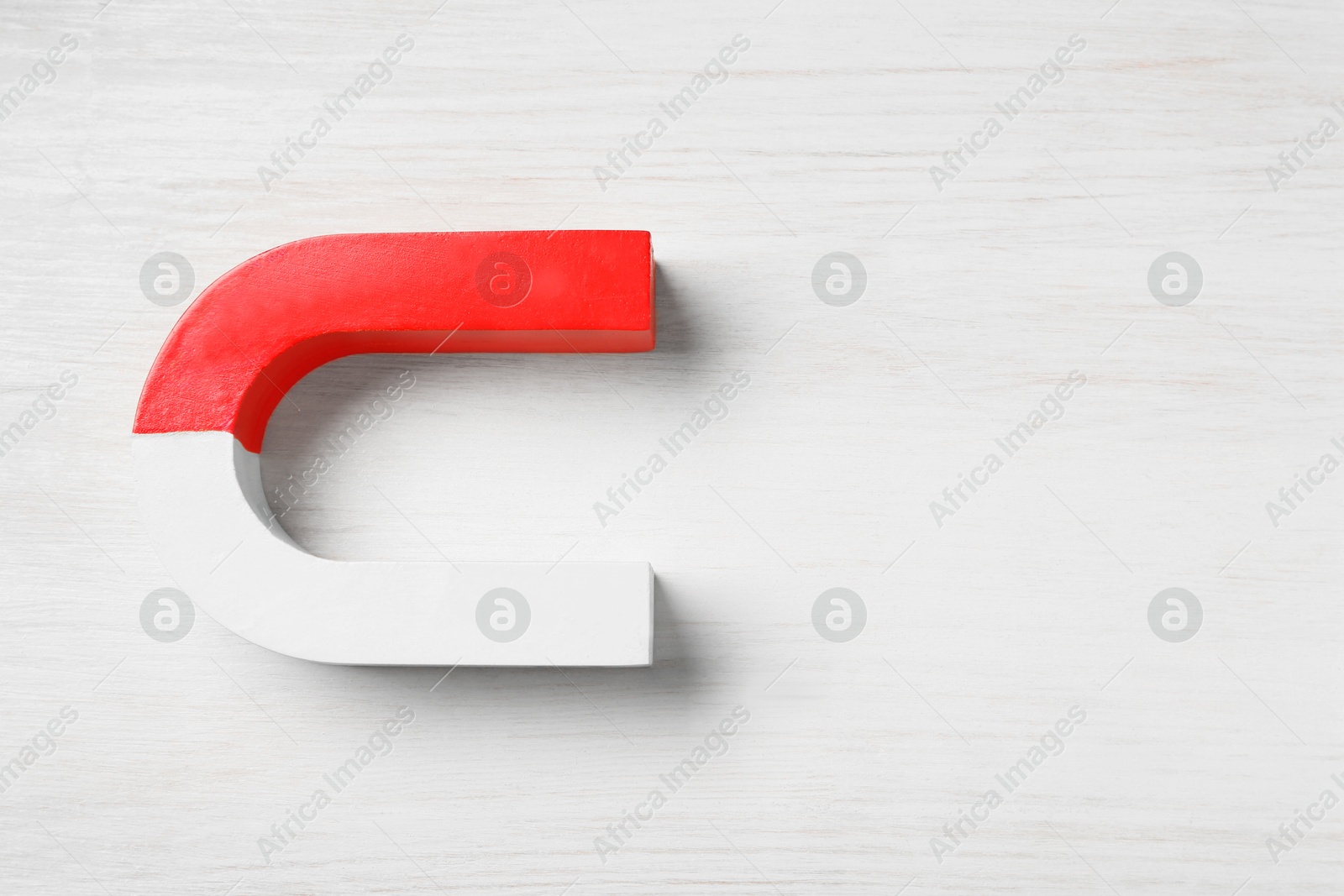 Photo of One horseshoe magnet on white wooden background, top view. Space for text