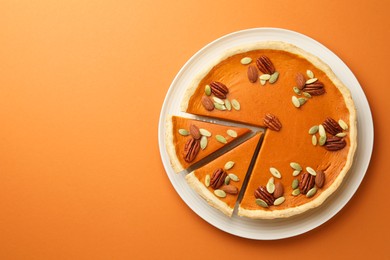 Photo of Tasty homemade pumpkin pie with seeds and nuts on orange background, top view. Space for text