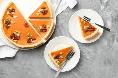 Photo of Pieces of tasty homemade pumpkin pie with seeds and nuts on grey table, top view