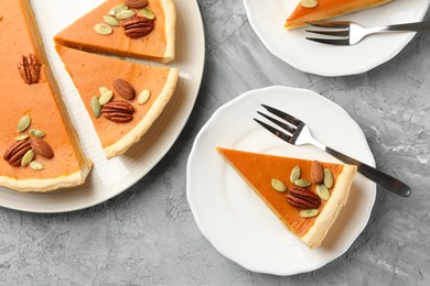 Photo of Pieces of tasty homemade pumpkin pie with seeds and nuts on grey table, top view