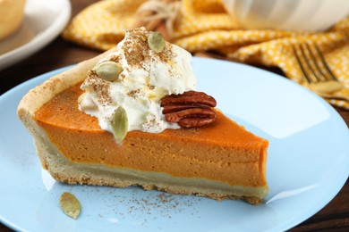 Photo of Piece of tasty homemade pumpkin pie with whipped cream, seeds and pecan nut on table, closeup