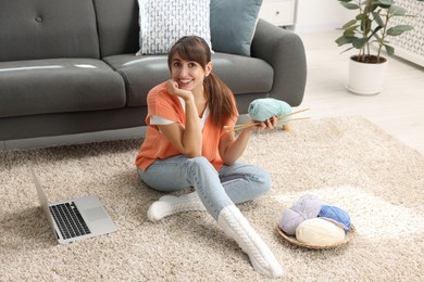 Photo of Beautiful woman learning to knit with online course on floor at home