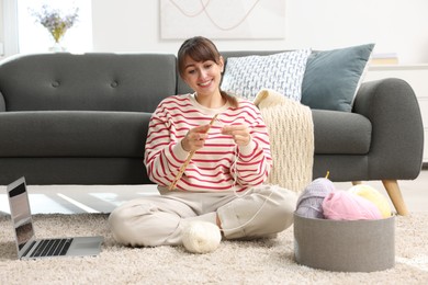 Beautiful woman learning to knit with online course on floor at home