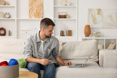 Man learning to knit with online course on sofa at home