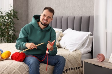 Photo of Man with colorful yarns and knitting needles on bed at home