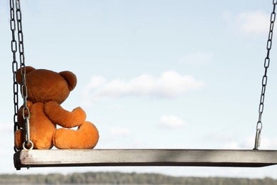 Photo of Lonely teddy bear on swing near river, back view