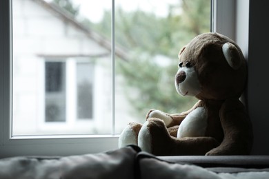 Photo of Lonely teddy bear near window. Space for text