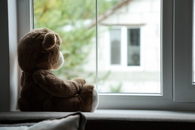 Photo of Lonely teddy bear near window. Space for text