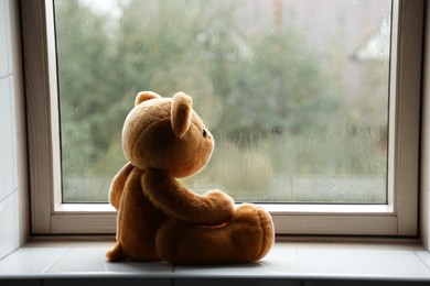 Photo of Lonely teddy bear near window on rainy day. Space for text