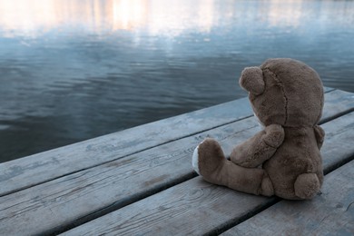 Photo of Lonely teddy bear on deck near river, space for text