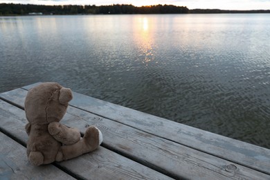 Photo of Lonely teddy bear on deck near river, space for text