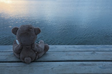 Photo of Lonely teddy bear on deck near river, back view. Space for text