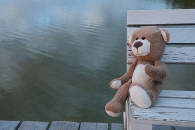 Photo of Lonely teddy bear on bench near river, space for text