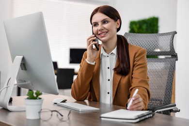 Photo of Woman talking on smartphone while working at table in office