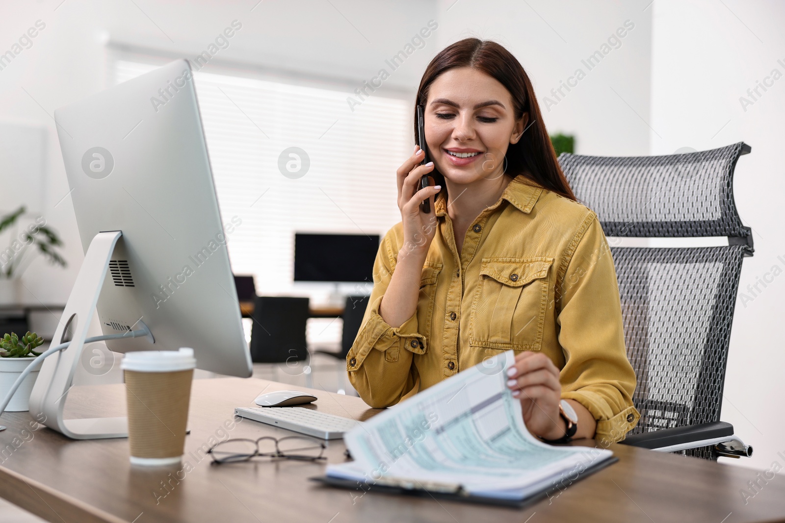 Photo of Woman talking on smartphone while working at table in office