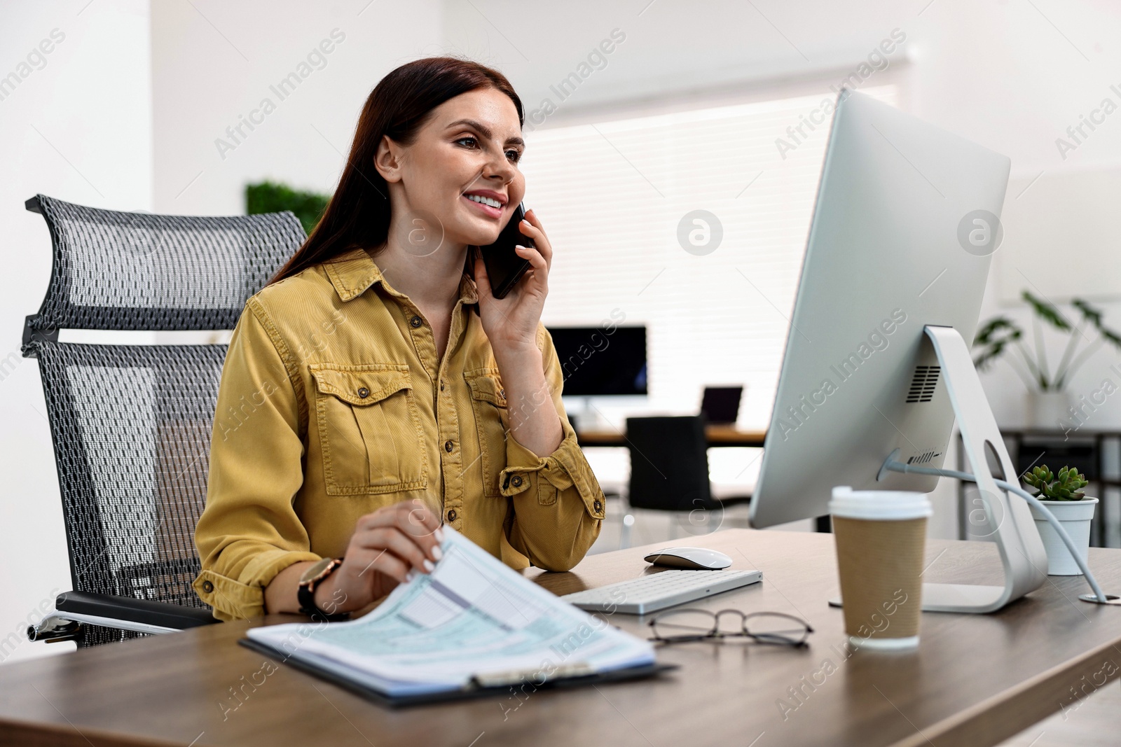 Photo of Woman talking on smartphone while working at table in office