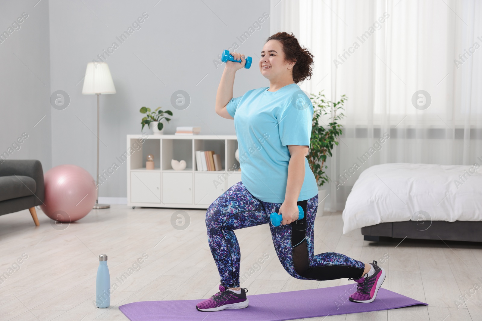 Photo of Plus size woman with dumbbells training at home