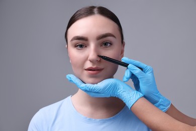 Photo of Doctor drawing marks on patient's nose for plastic surgery operation against grey background, closeup