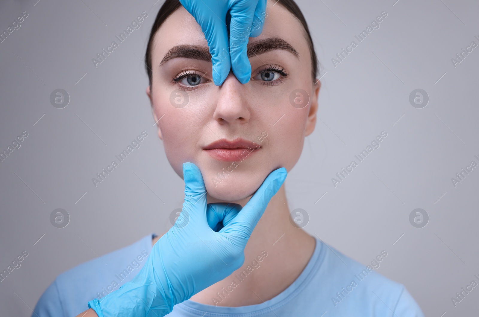 Photo of Doctor checking patient's nose before plastic surgery operation on grey background, closeup