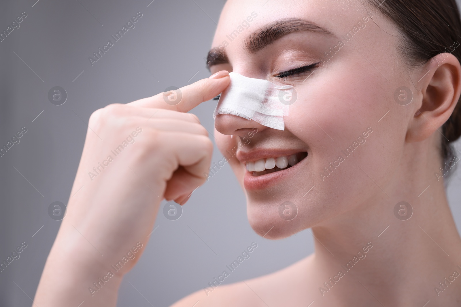 Photo of Woman with medical bandage on her nose after plastic surgery operation against grey background