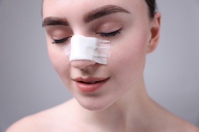 Photo of Woman with medical bandage on her nose after plastic surgery operation against grey background