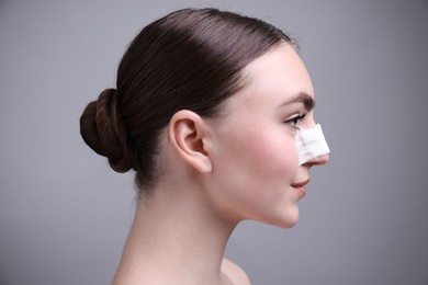 Photo of Woman with medical bandage on her nose after plastic surgery operation against grey background