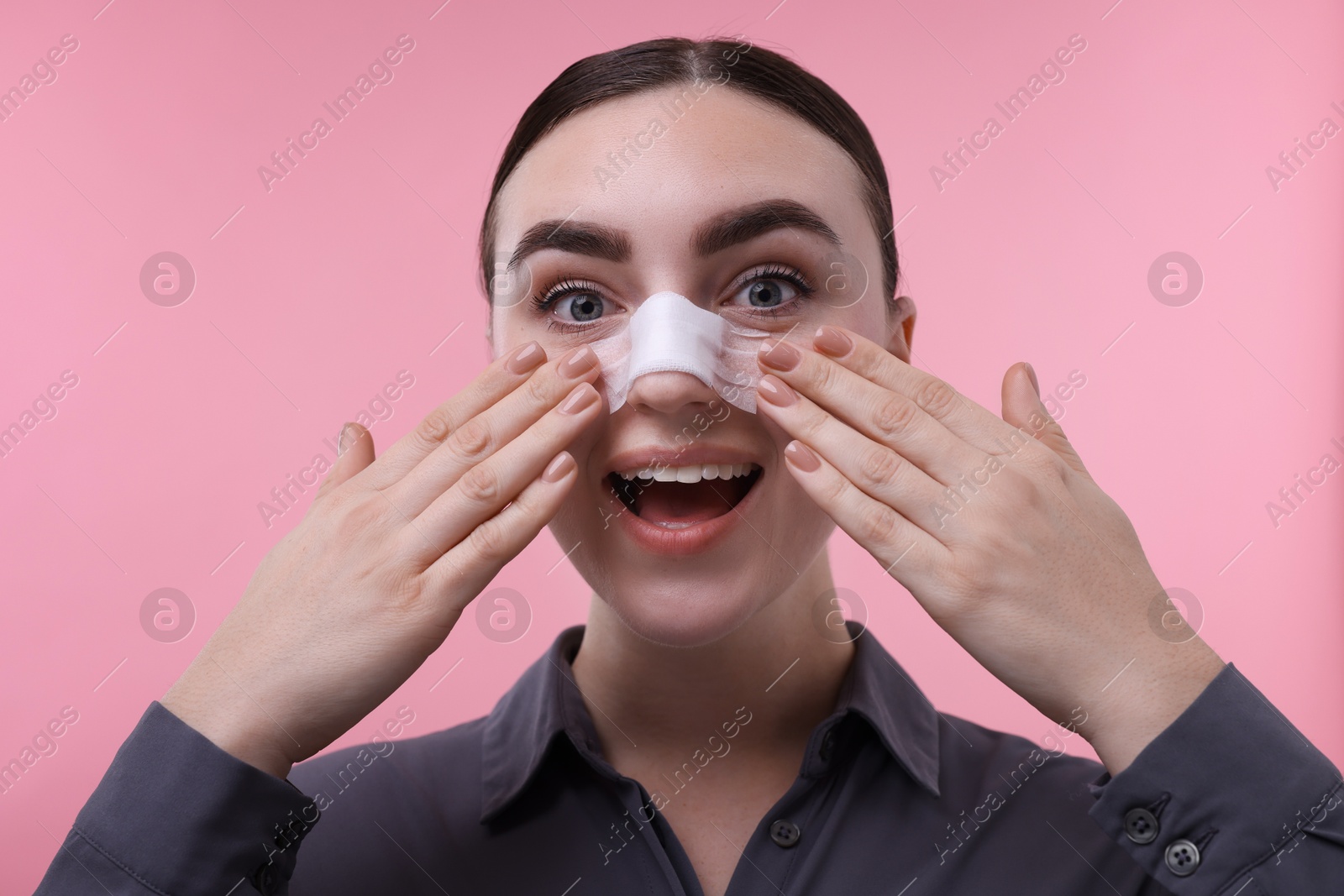 Photo of Woman with medical bandage on her nose after plastic surgery operation against pink background