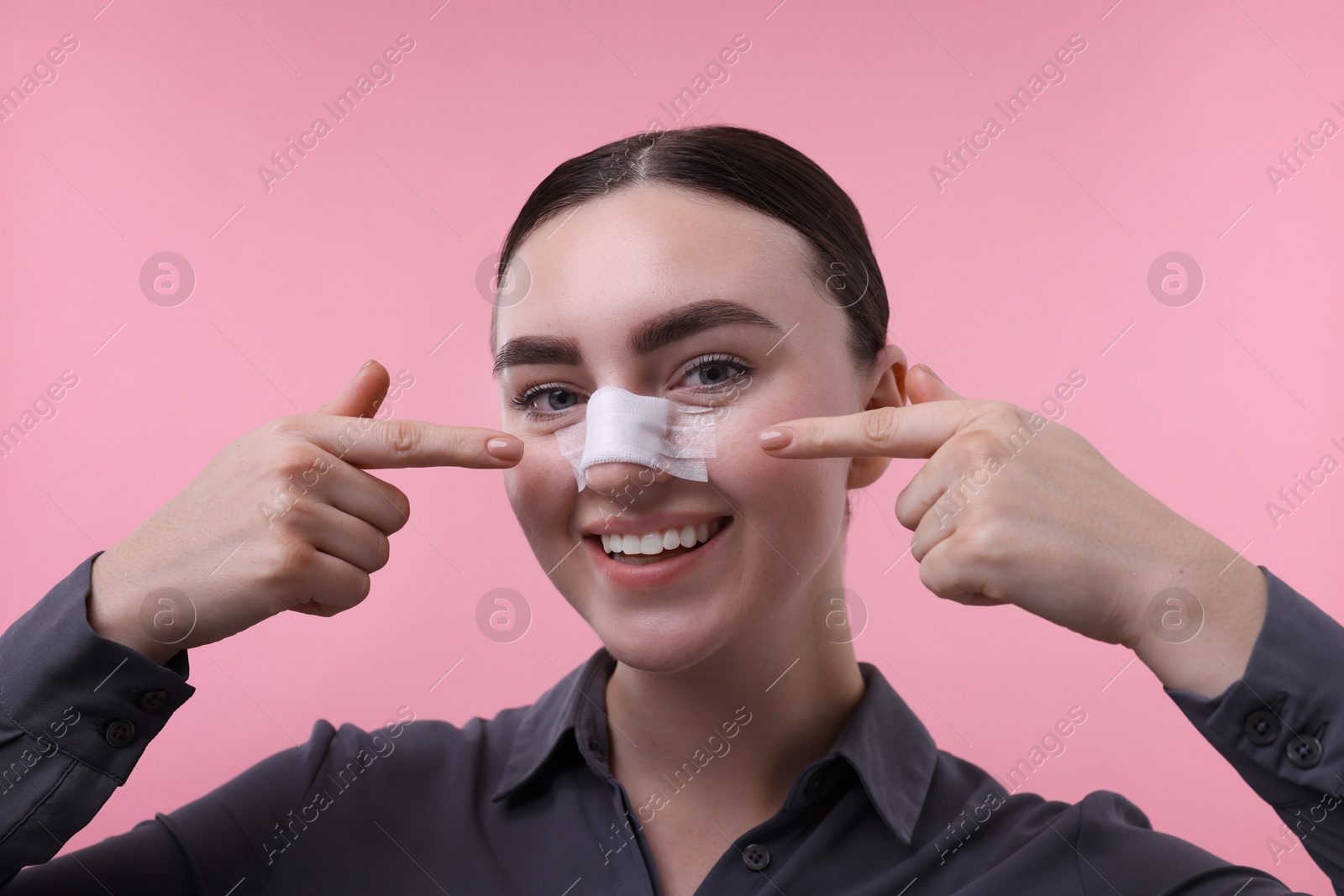 Photo of Woman with medical bandage on her nose after plastic surgery operation against pink background