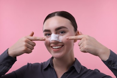 Photo of Woman with medical bandage on her nose after plastic surgery operation against pink background