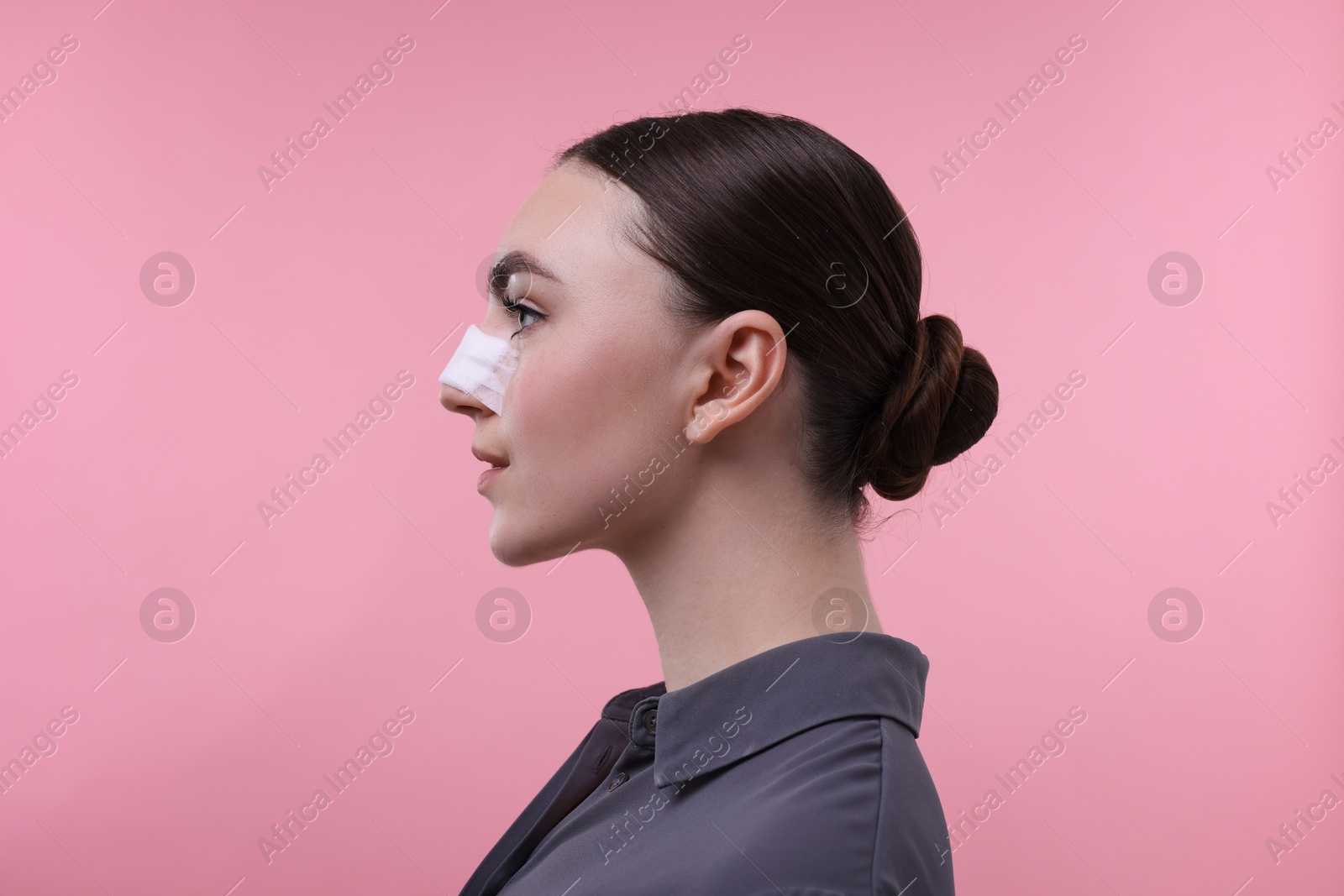 Photo of Woman with medical bandage on her nose after plastic surgery operation against pink background