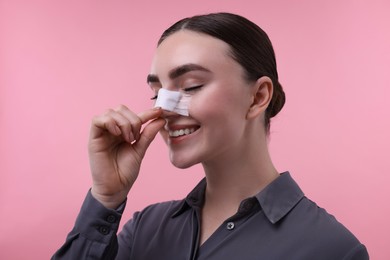 Photo of Woman with medical bandage on her nose after plastic surgery operation against pink background