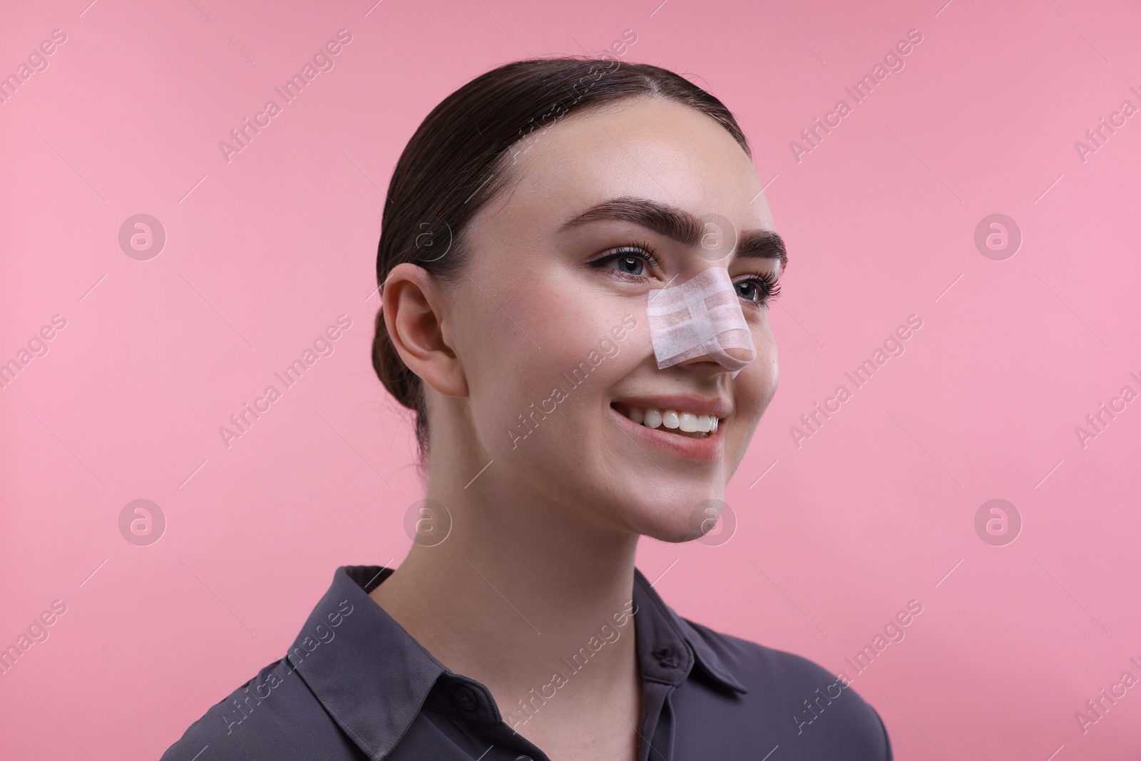 Photo of Woman with medical bandage on her nose after plastic surgery operation against pink background