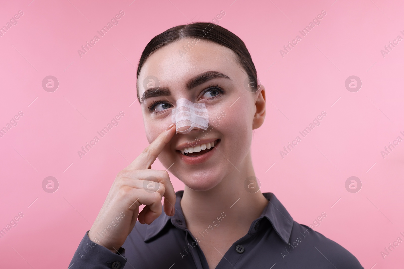 Photo of Woman with medical bandage on her nose after plastic surgery operation against pink background