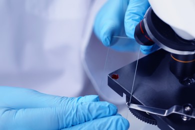 Scientist examining sample on slide under microscope, closeup