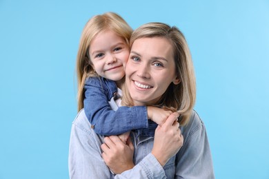 Photo of Cute little girl hugging her mom on light blue background. Happy Mother's Day