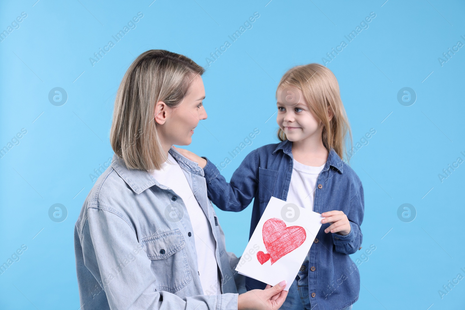 Photo of Little daughter congratulating her mom with greeting card on light blue background. Happy Mother's Day