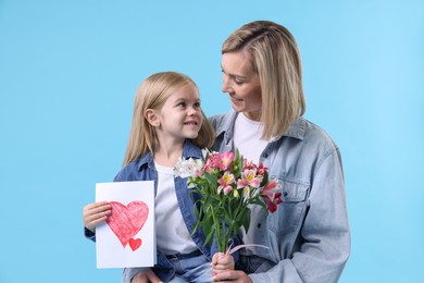 Photo of Little daughter congratulating her mom with bouquet of alstroemeria flowers and greeting card on light blue background. Happy Mother's Day