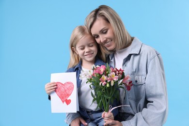 Photo of Little daughter congratulating her mom with bouquet of alstroemeria flowers and greeting card on light blue background. Happy Mother's Day