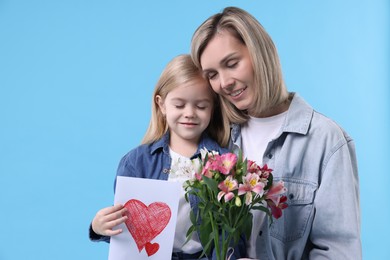 Photo of Little daughter congratulating her mom with bouquet of alstroemeria flowers and greeting card on light blue background, space for text. Happy Mother's Day