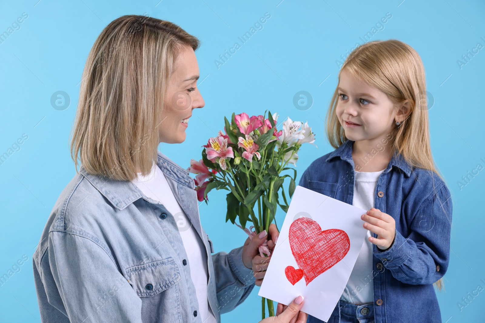 Photo of Little daughter congratulating her mom with bouquet of alstroemeria flowers and greeting card on light blue background. Happy Mother's Day