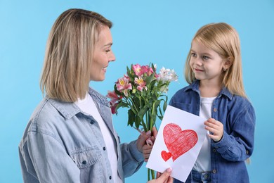 Photo of Little daughter congratulating her mom with bouquet of alstroemeria flowers and greeting card on light blue background. Happy Mother's Day