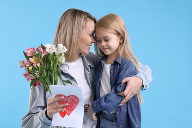 Photo of Little daughter congratulating her mom with bouquet of alstroemeria flowers and greeting card on light blue background. Happy Mother's Day