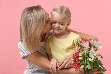 Little daughter congratulating her mom with bouquet of alstroemeria flowers on pink background. Happy Mother's Day