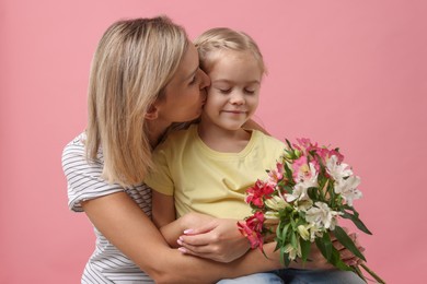 Little daughter congratulating her mom with bouquet of alstroemeria flowers on pink background. Happy Mother's Day