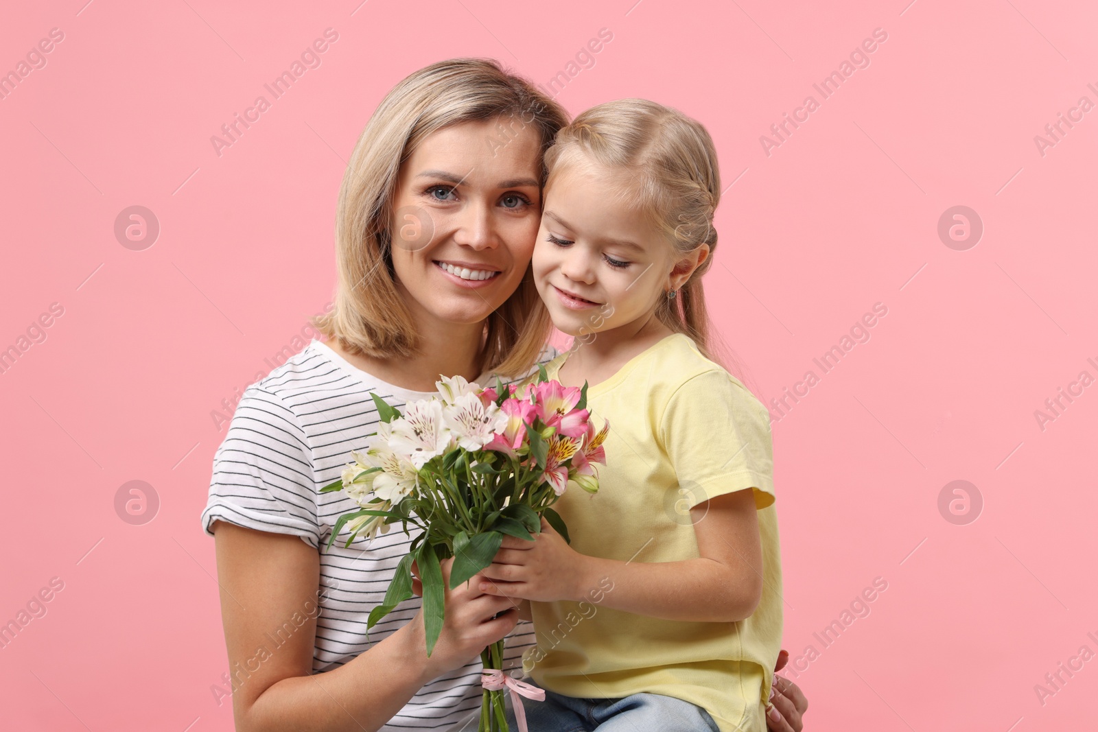 Photo of Little daughter congratulating her mom with bouquet of alstroemeria flowers on pink background. Happy Mother's Day