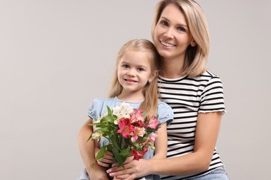 Photo of Happy woman with her daughter and bouquet of alstroemeria flowers on gray background. Mother's Day celebration